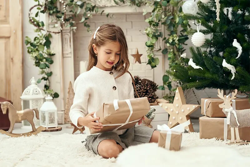 Niña abriendo un regalo durante una sesión de fotos de Navidad en estudio.