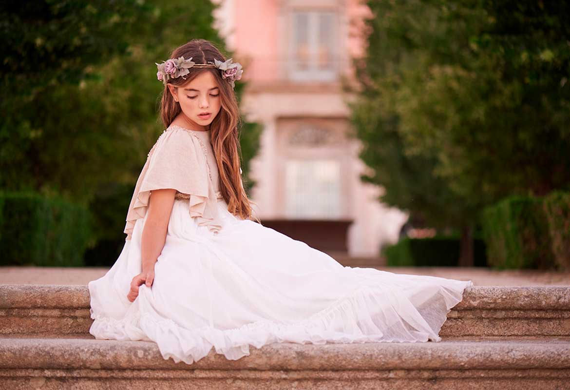 Niña con corona de flores y vestido de comunión sentada en las escaleras durante sesión en Madrid.