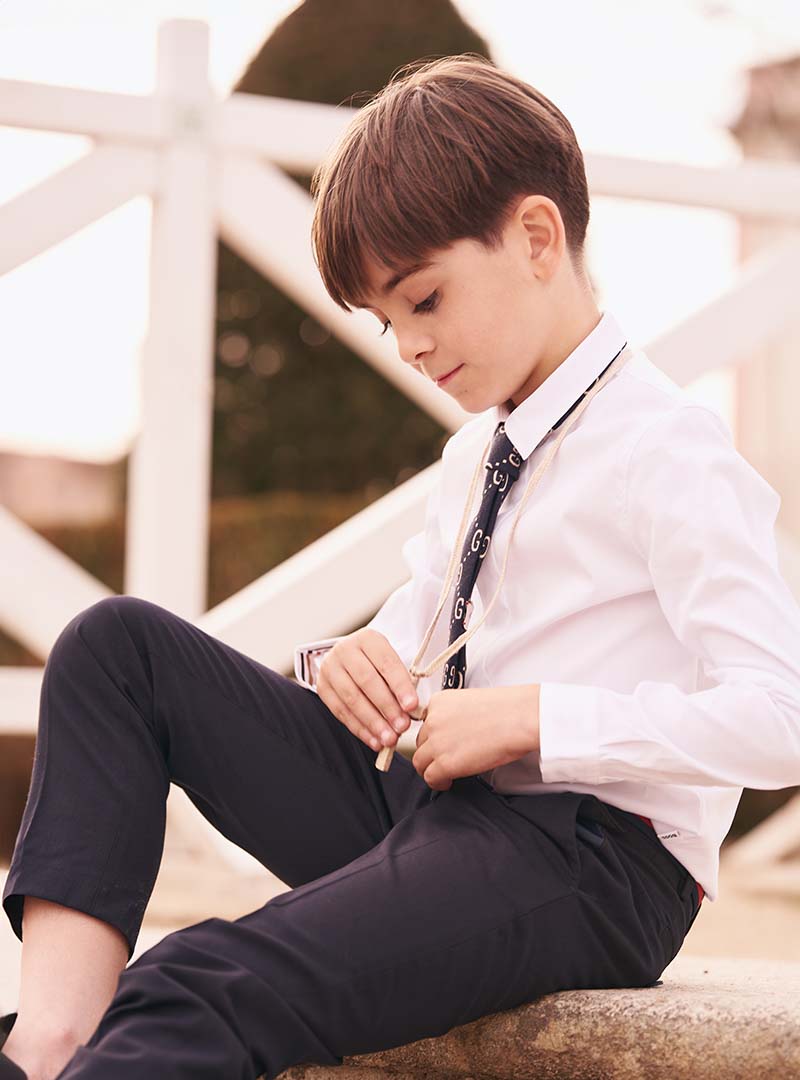 Niño con camisa blanca y corbata negra sentado en una escalera durante sesión de comunión en Madrid.