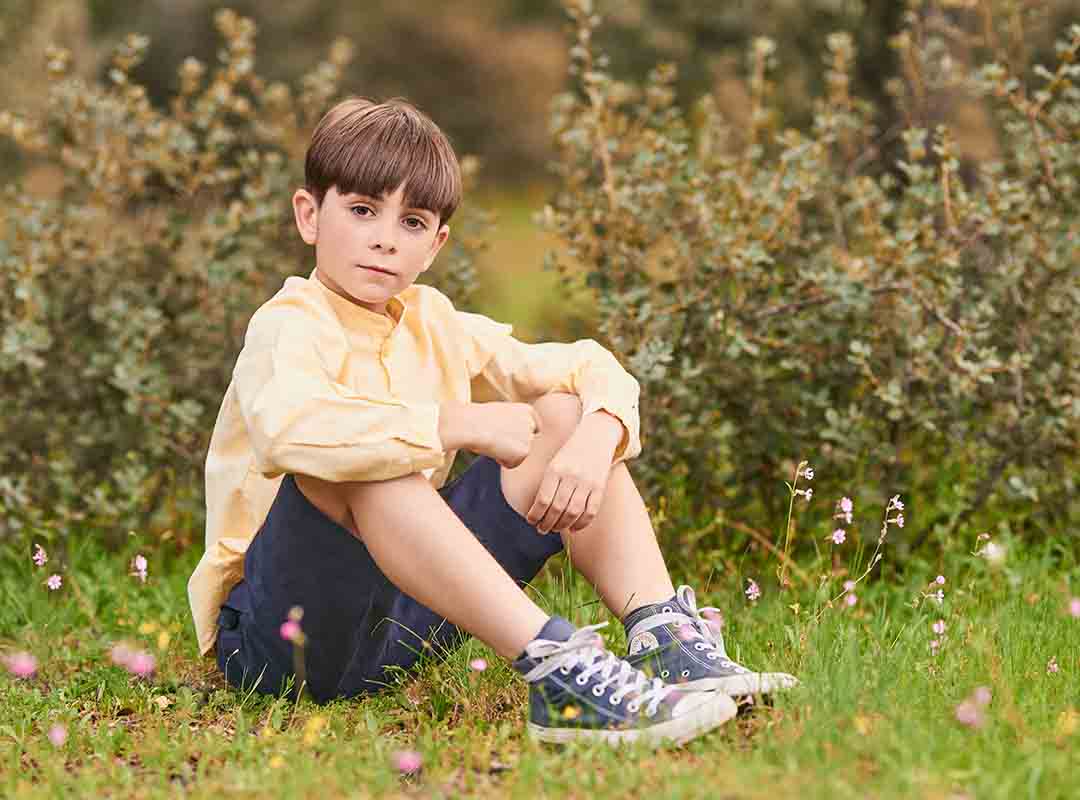 Niño con camisa amarilla y pantalón azul posando en el césped durante sesión de comunión en Madrid.