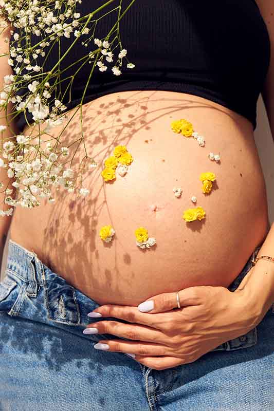 Sesión de fotos de embarazo con decoración floral en Madrid Mujer embarazada con flores en la barriga posando para una sesión de fotos en Madrid.