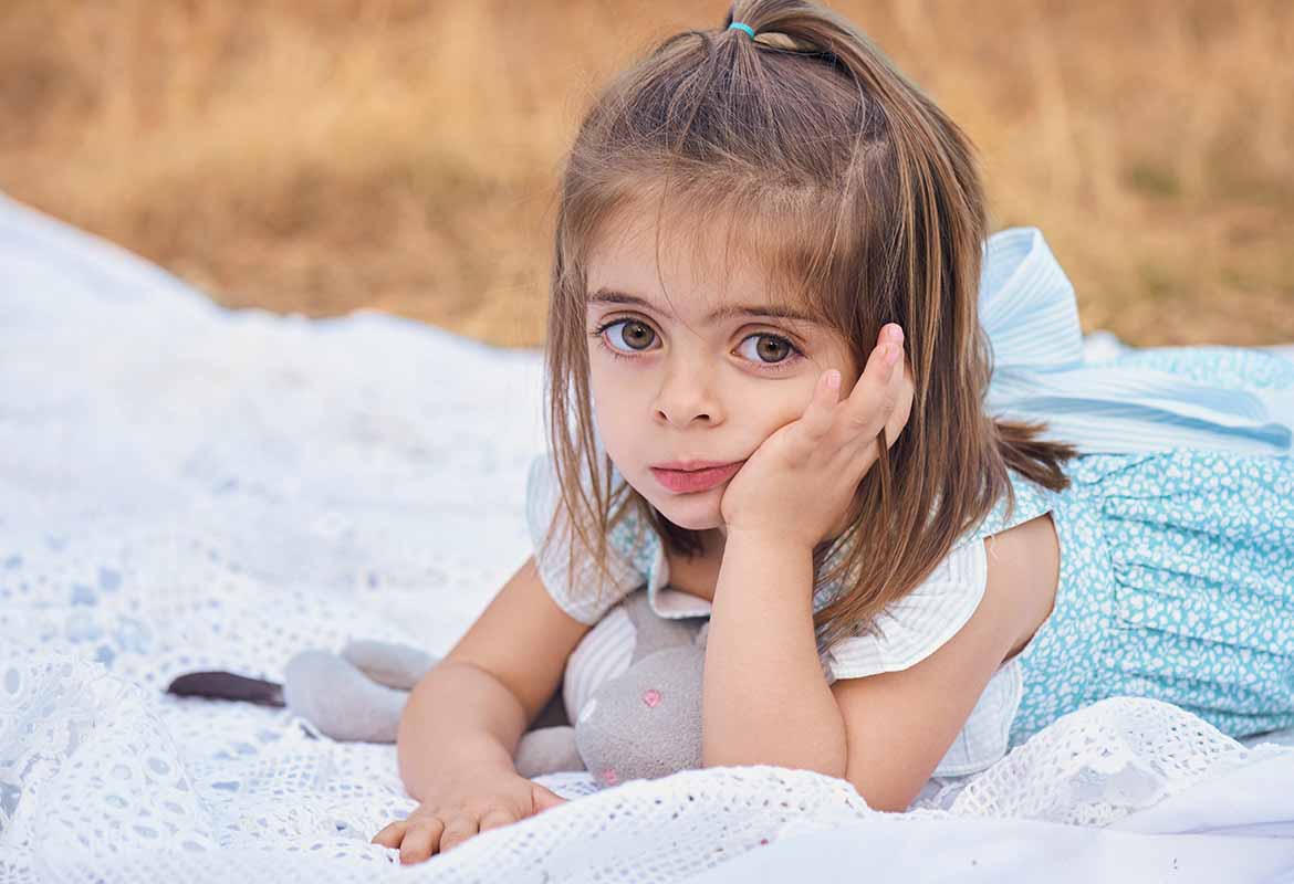 Sesión de fotos de niña con vestido azul en el campo en Madrid Sesión de fotos en Madrid de niña pensativa con vestido azul sobre una manta en el campo.